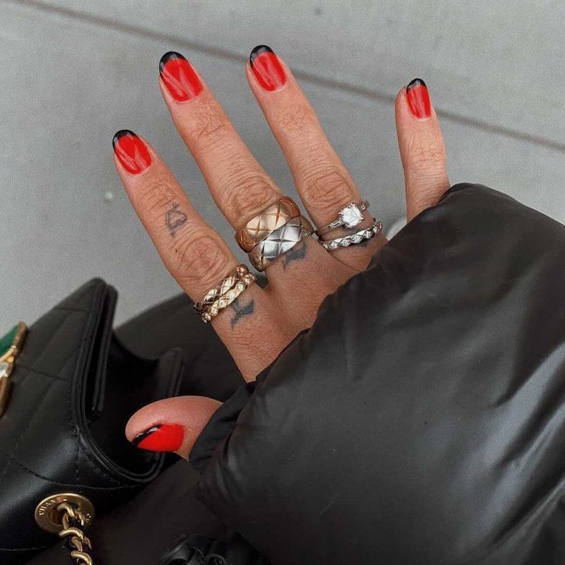 Manicure vermelha com dicas francesas negras e anéis colocados feitos de metais mistos