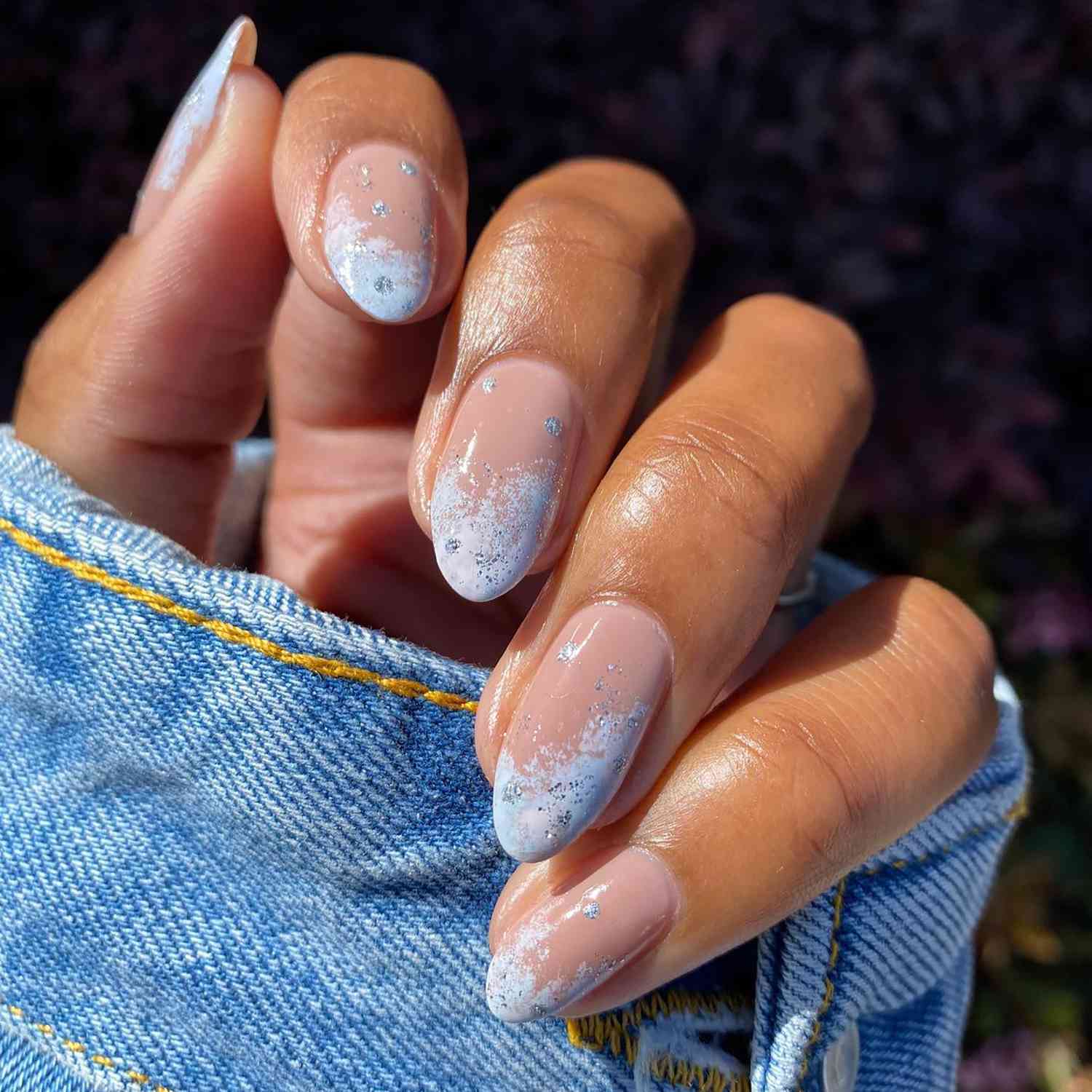 Uma manicure de close-up com pontas azuis de neve e pontos prateados brilhantes