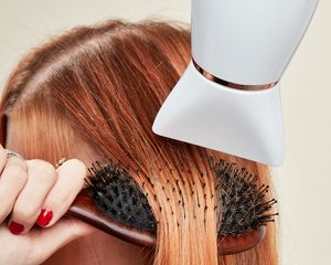 Close-up de uma mulher penteando o cabelo ruivo enquanto seca o cabelo