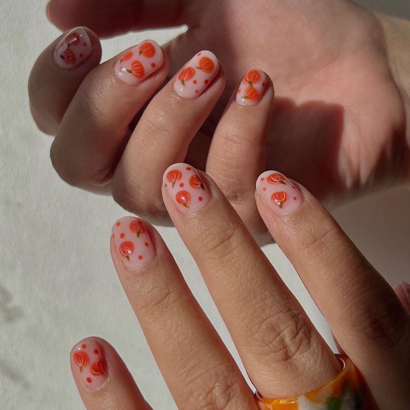 Manicure neutra com pequenos desenhos de abóbora e pontos laranja em bolinhas