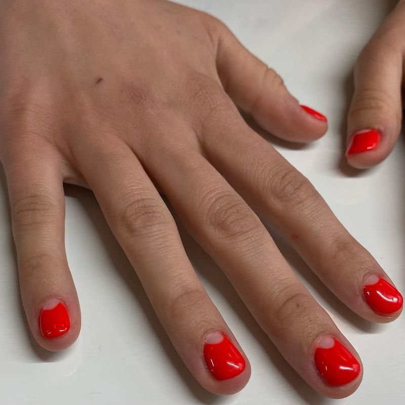 Manicure em laranja vermelha com o design de unhas na forma de um crescente com um espaço negativo