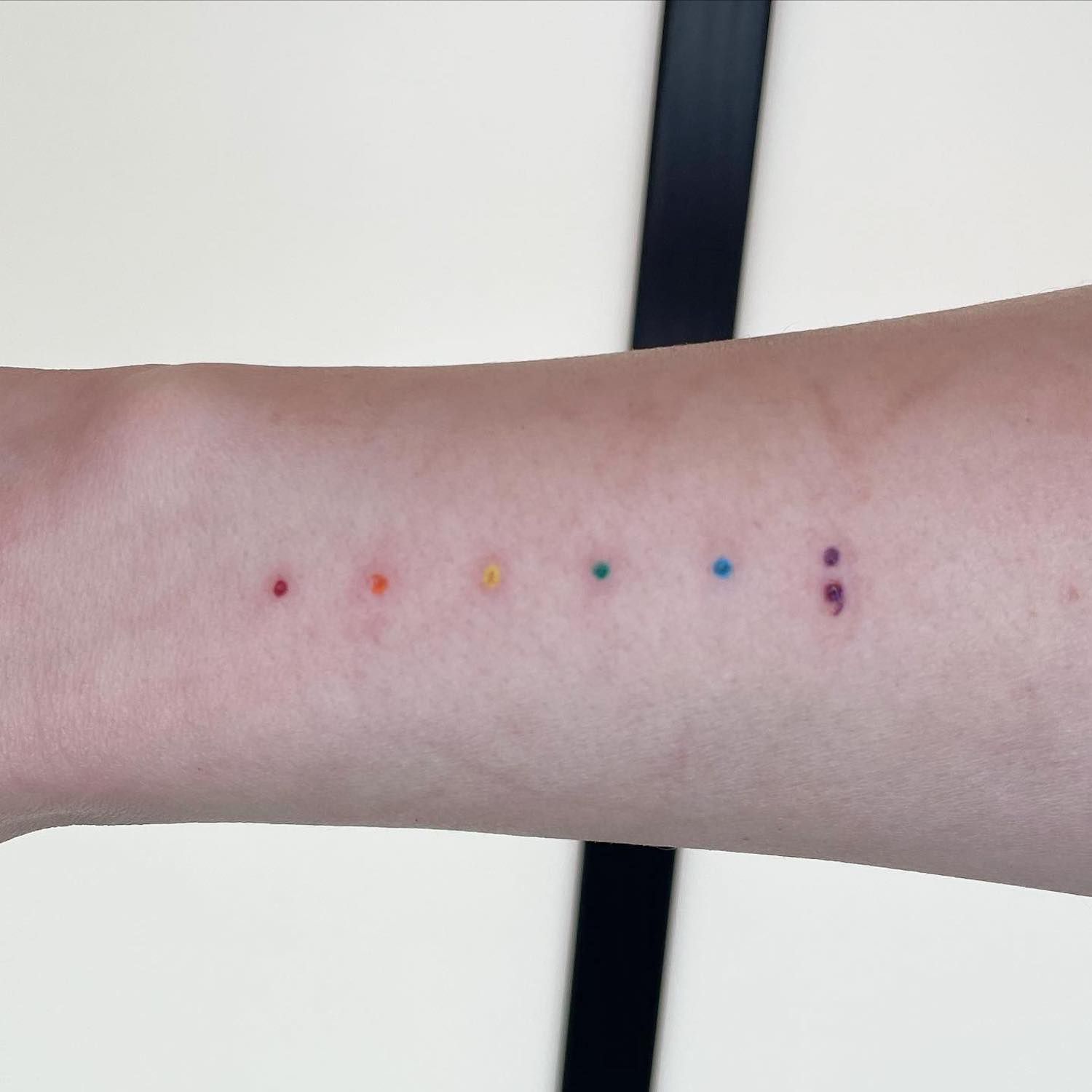 Mão com uma tatuagem na forma de pontos de arc o-íris com um ponto roxo com uma vírgula