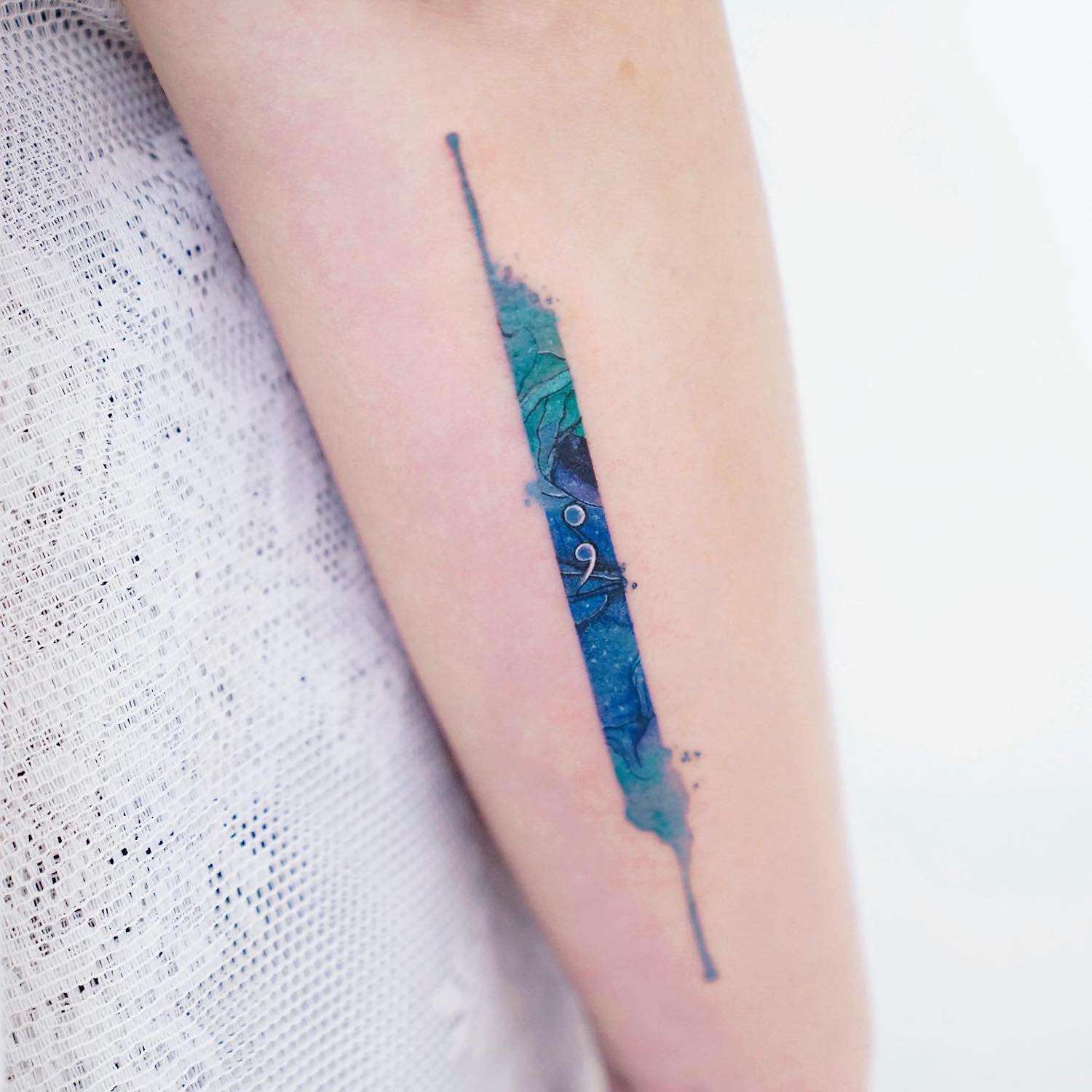 Mão com uma tatuagem em aquarela azul e verde com uma imagem de uma longa