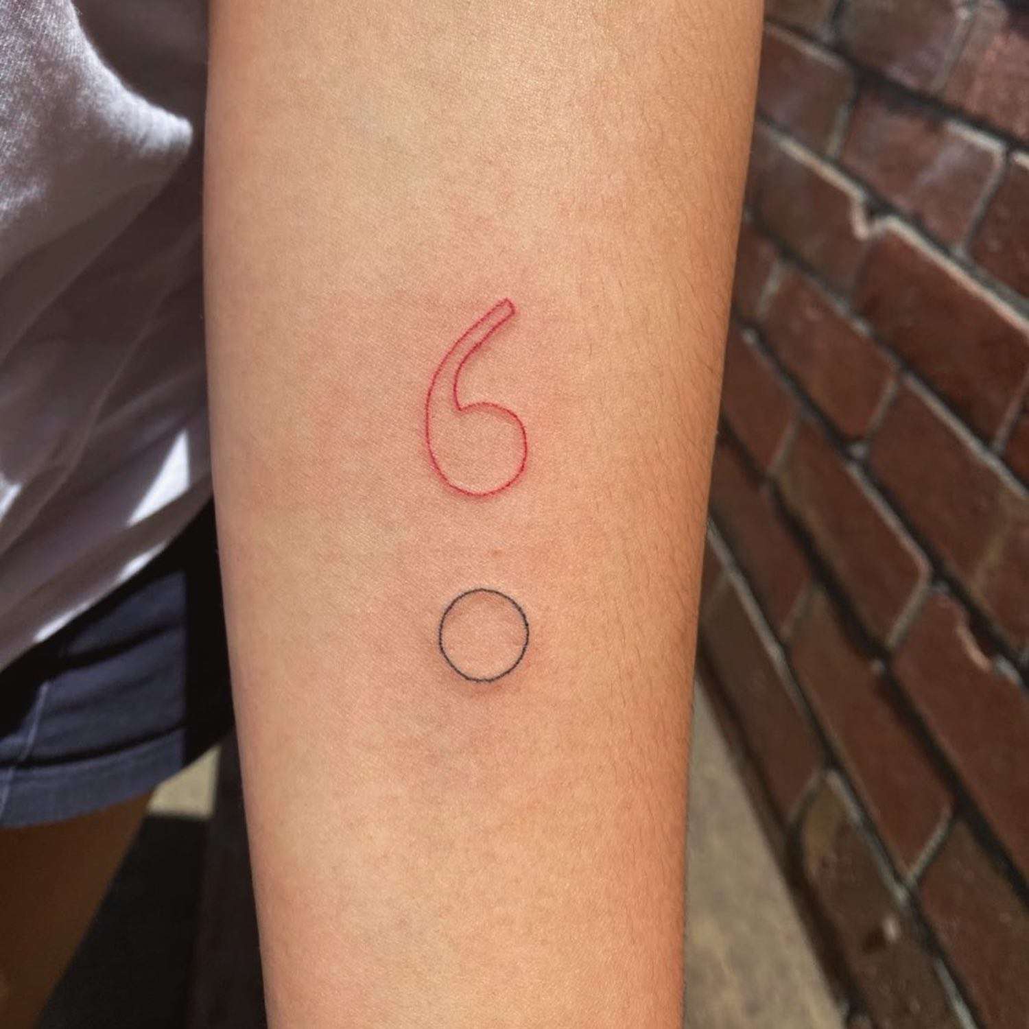 Mão com uma tatuagem vermelha e preta fina na forma de um ponto com uma vírgula