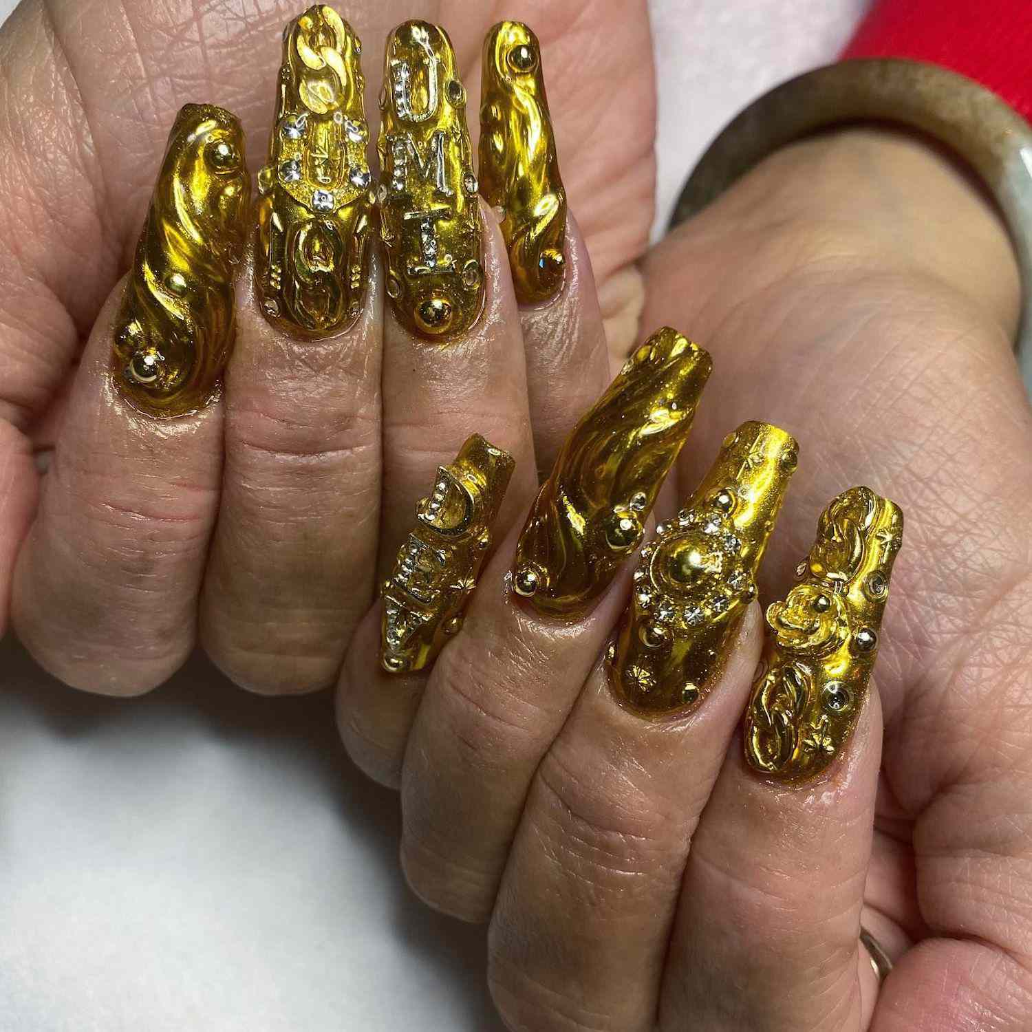 Manicure dourada com um design 3D de metal e dicas quadradas longas