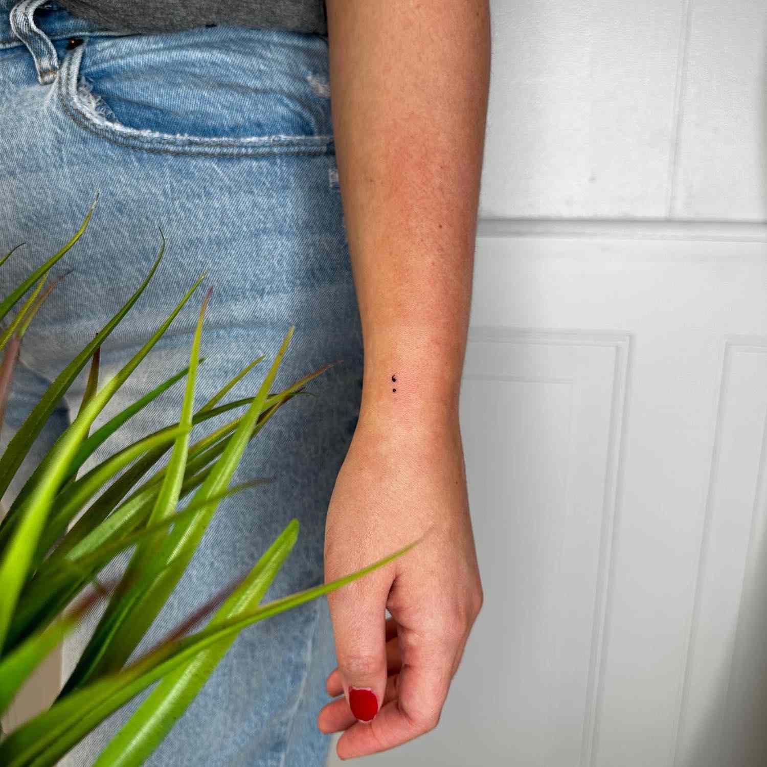 Micro tatuagem na forma de uma vírgula no pulso ao lado de jeans e planta