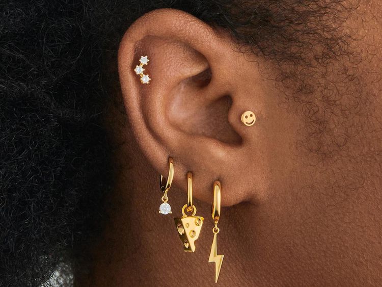 Close da orelha de uma mulher com muitos piercings dourados diferentes
