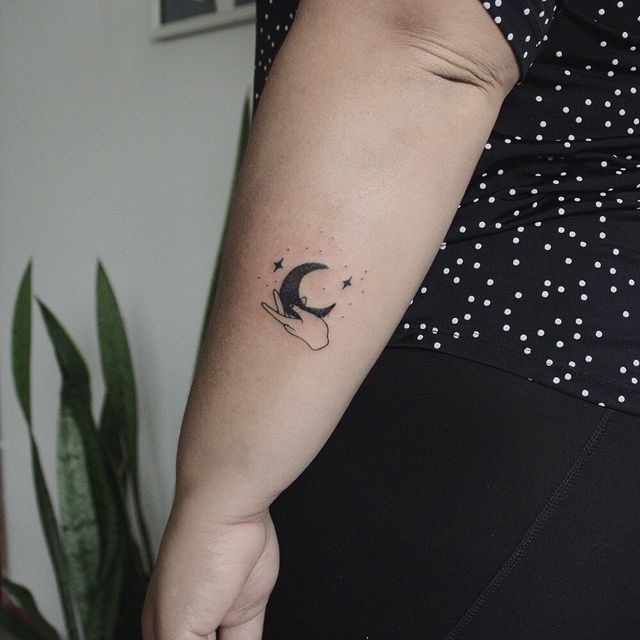 mão segurando a parte inferior de uma tatuagem de lua crescente