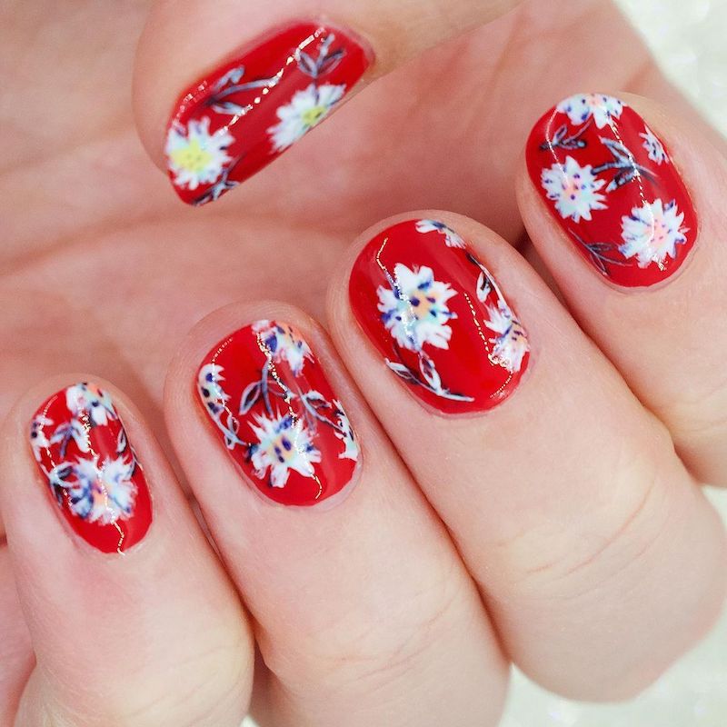 Manicure vermelha com detalhes brancos do design floral
