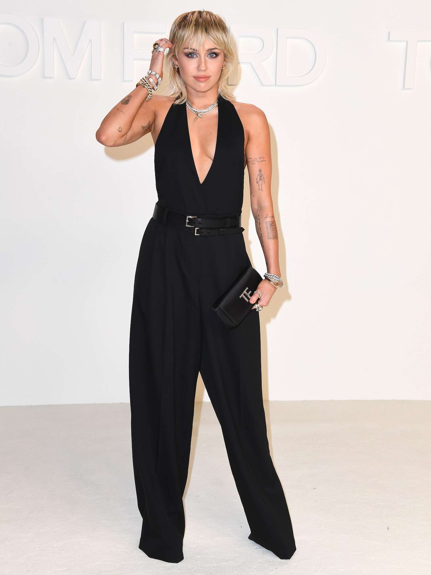 Miley Cyrus em um macacão preto com um decote profundo no show de Tom Ford outono 2020