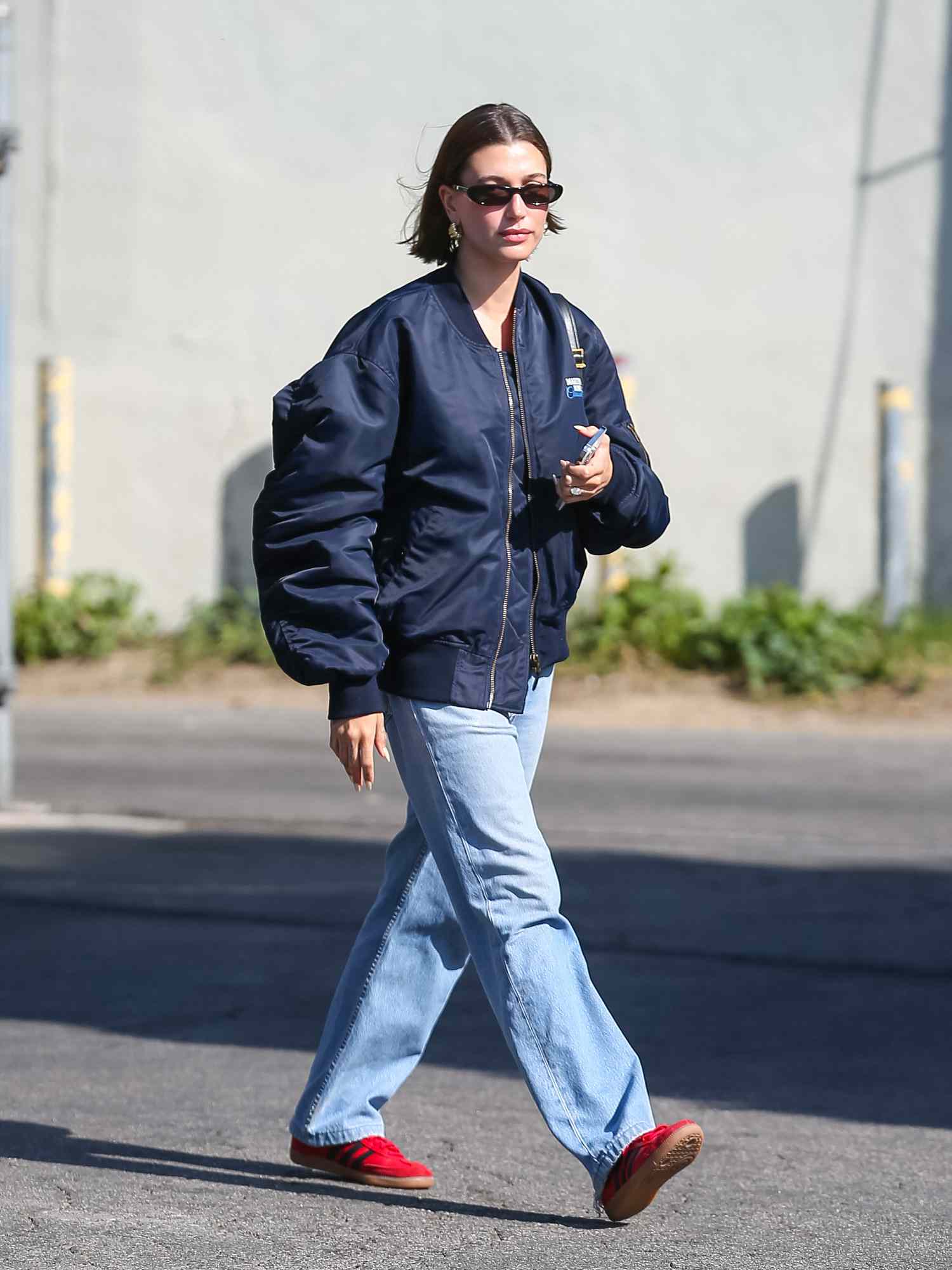 Haley Bieber em uma jaqueta de bombardeiro azul com jeans e tênis vermelhos adidas samba < man> influenser Lucy Williams em um suéter marrom, jeans, bolsas vermelhas e tênis pretos adidas samba