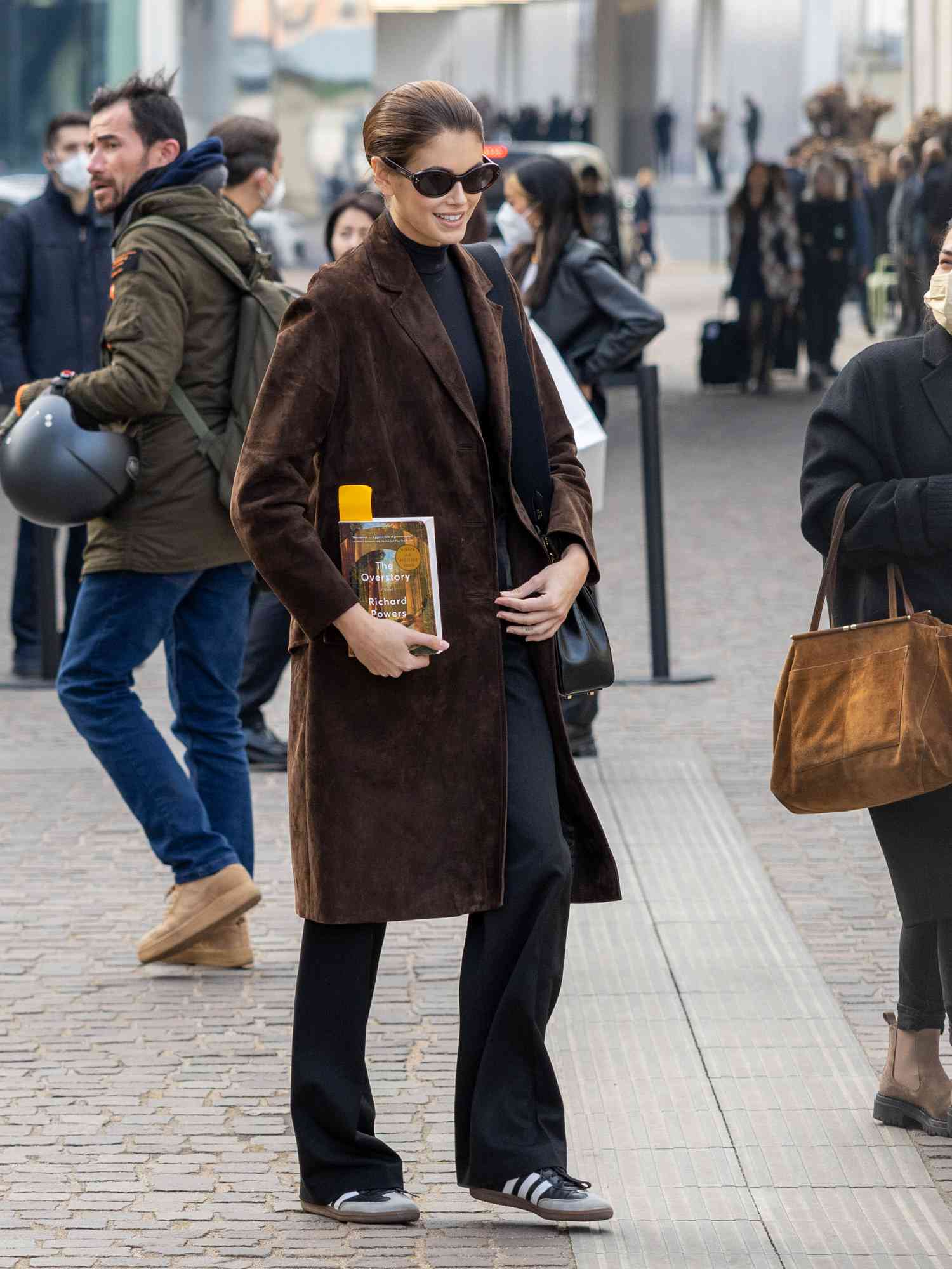 Kaya Herber em um longo casaco de camurça marrom com calças pretas e samks pretos adidas