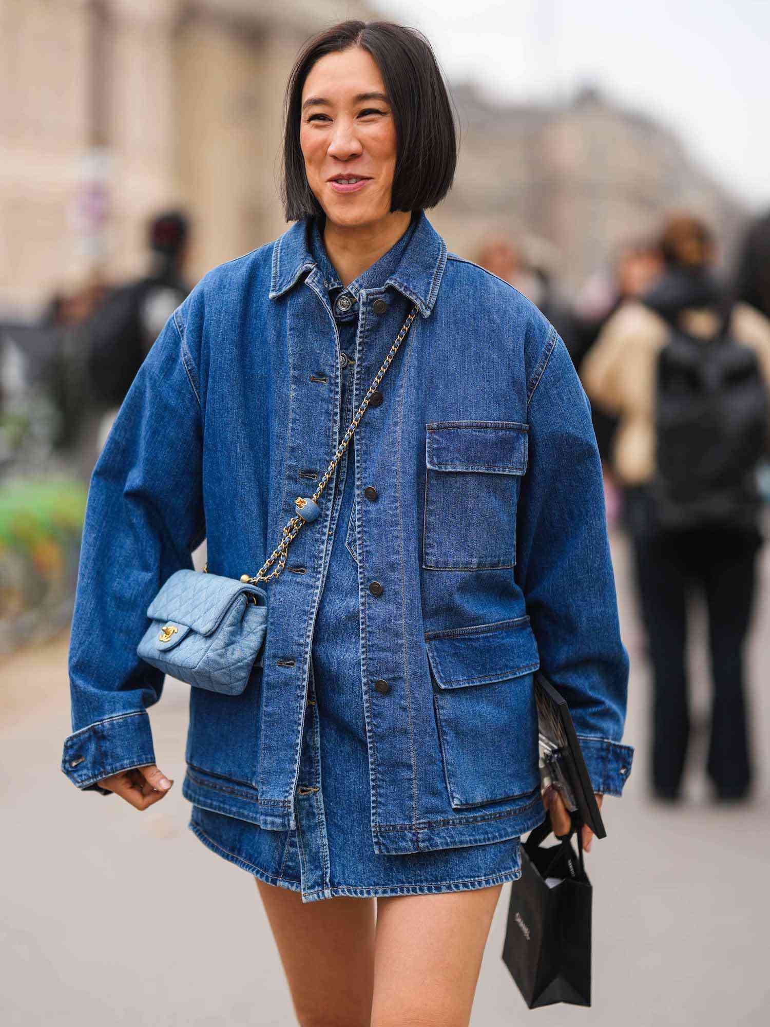 Eva Chen usa um cargo de jaqueta de jeans, um vestido de jeans com botões, uma bolsa azul Chanel Crossbody e uma bolsa de compra Chanel