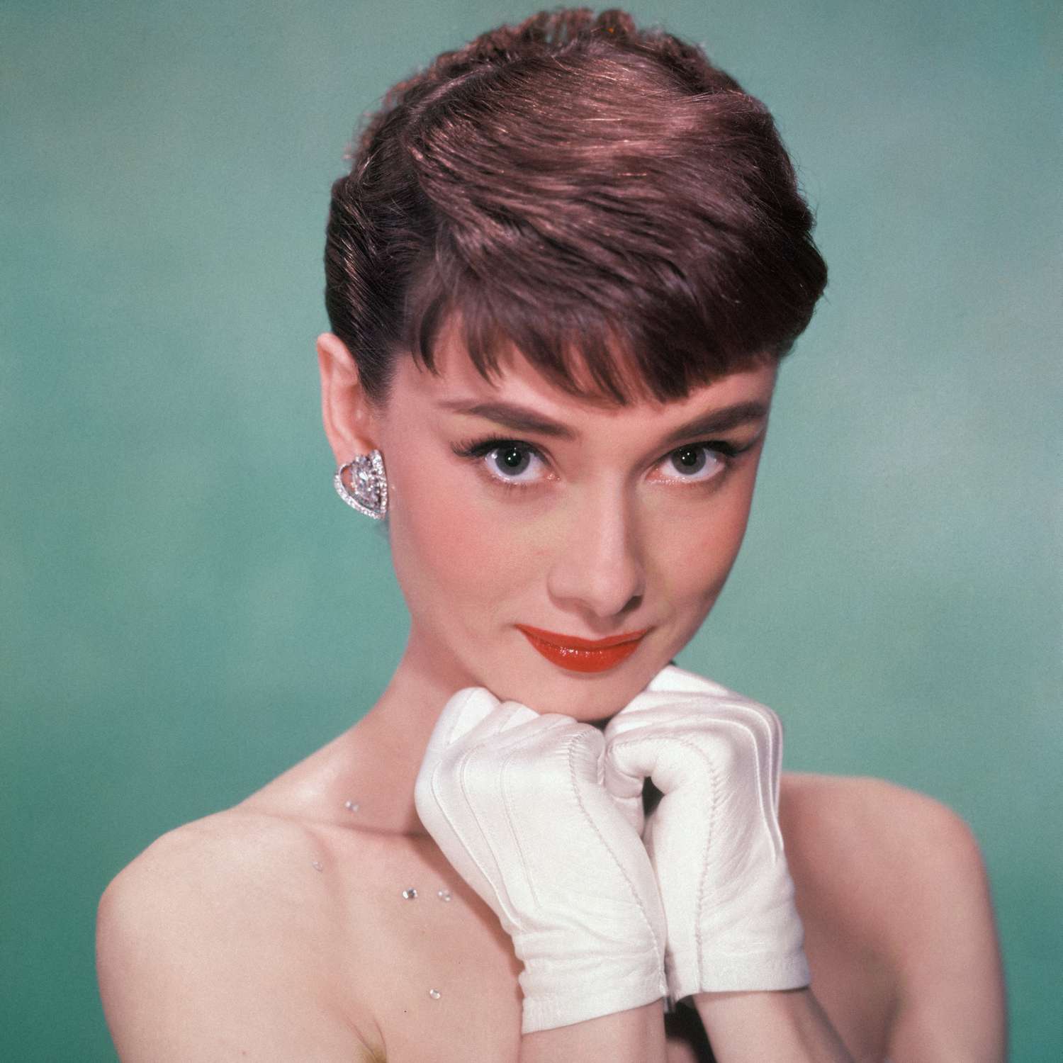 Audrey Hepburn em um vestido sem alças e mãos brancas com luvas de bebê na altura do queixo, início de 1950