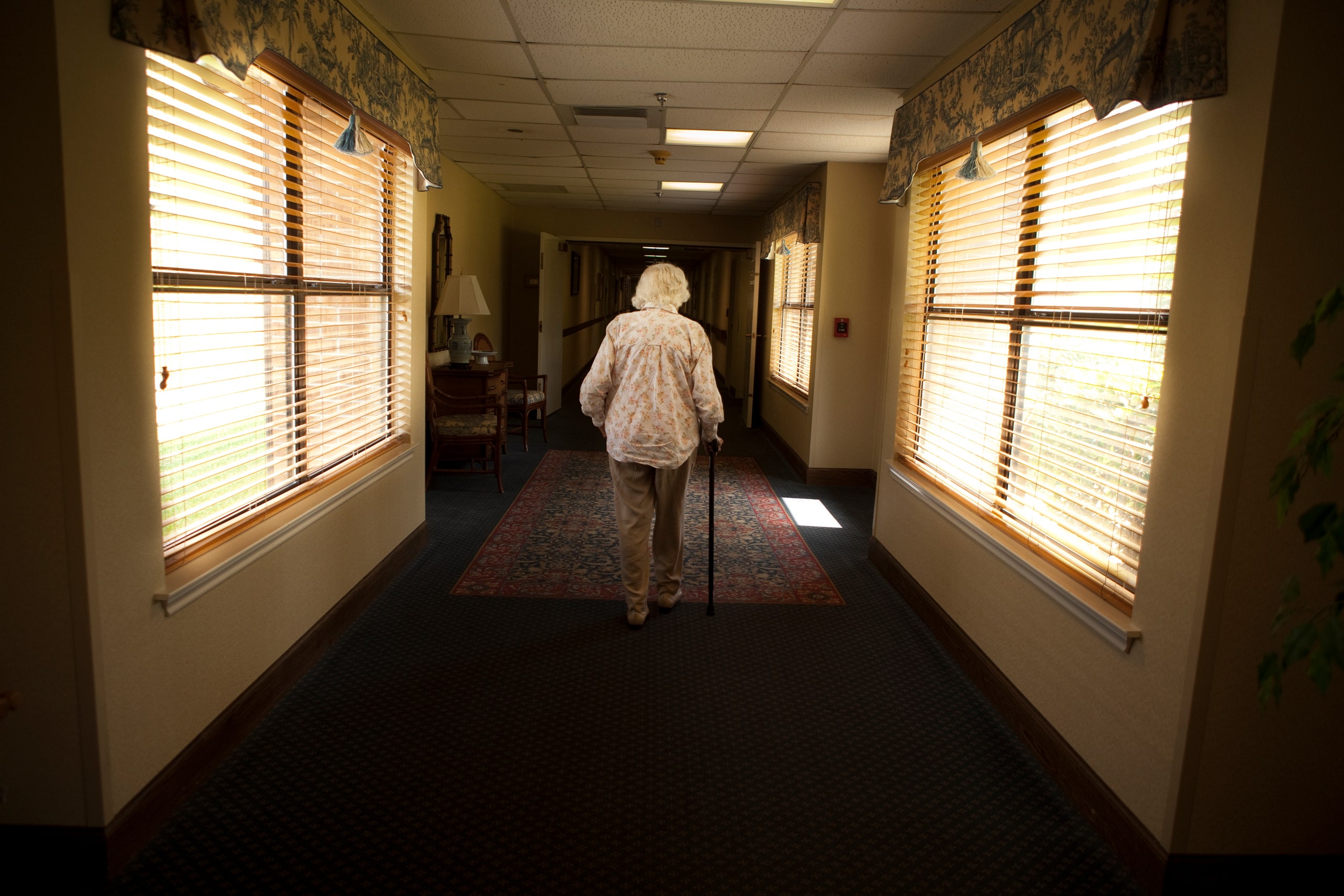 Uma mulher idosa caucasiana vai com uma bengala no lar de idosos