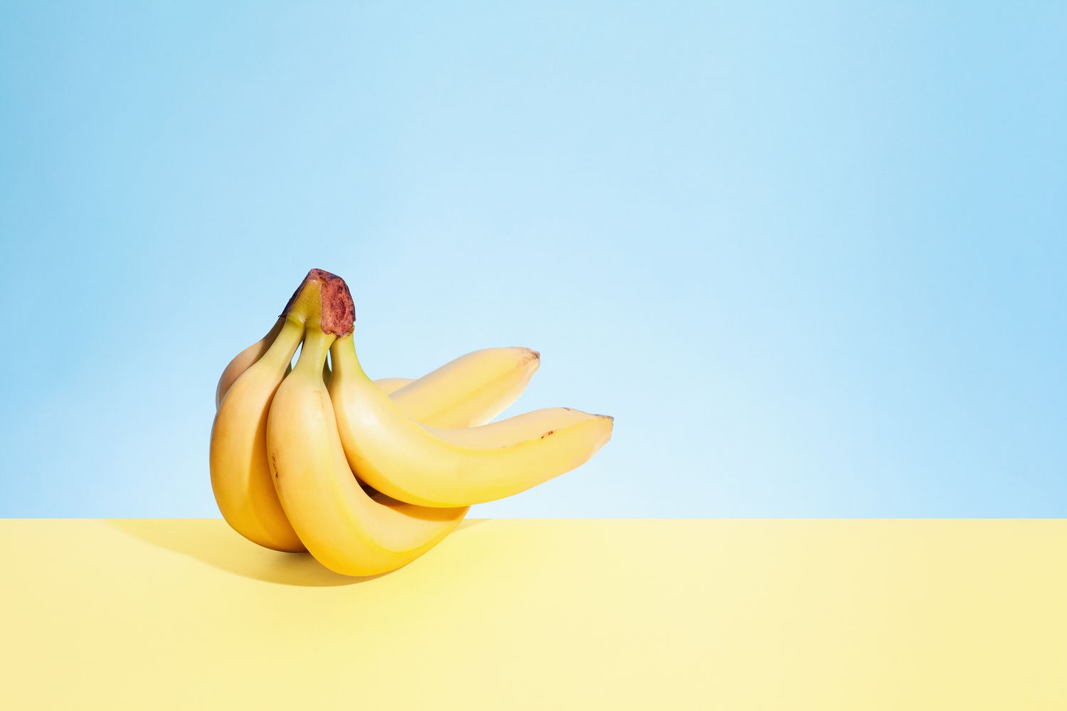 Um cacho de bananas sobre um fundo azul claro e amarelo claro.