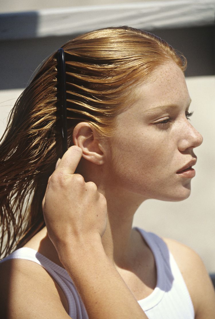 Uma mulher de cabelos vermelhos pega seus cabelos nos raios do sol.