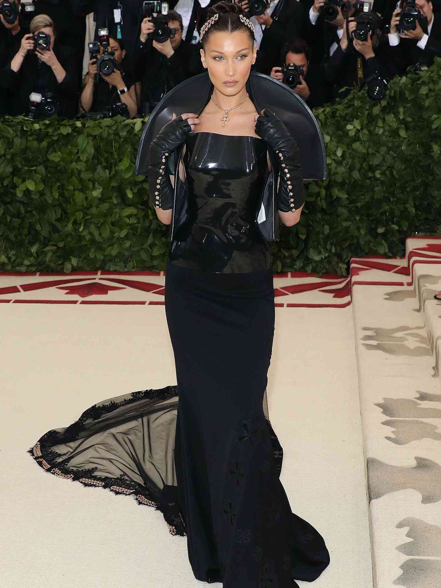 Bella Hadid em um vestido de corações cromados pretos com um trem, um top de couro envernizado e pontas dos dedos no Met Gala 2018