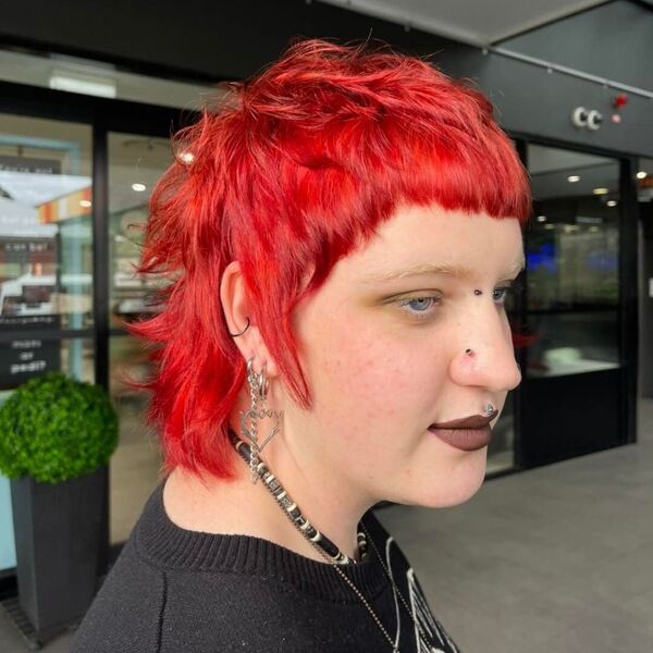 Cortes de cabelo de tainha vermelha ousada - uma mulher usa muitos brincos e um colar