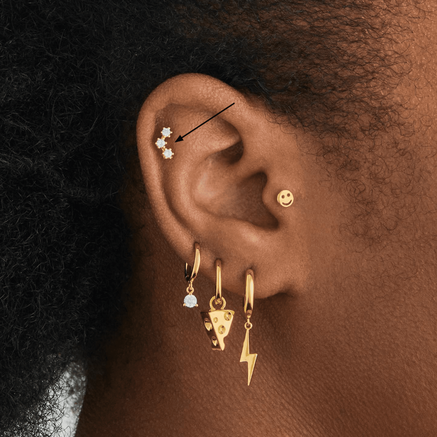 Vista lateral da orelha de uma mulher com muitos piercings dourados