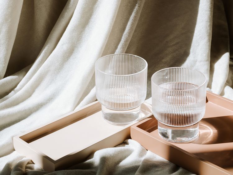 Dois copos de água em bandejas com tecido texturizado em segundo plano