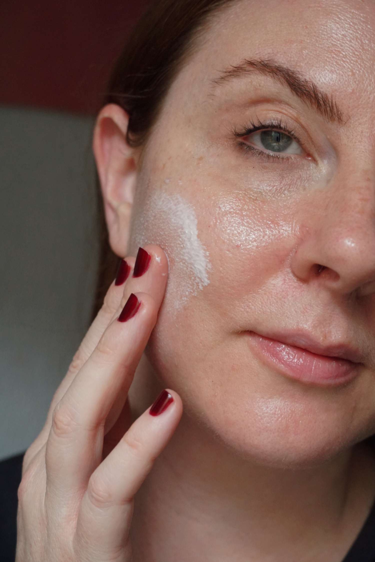 Uma mulher aplica um creme no rosto sem maquiagem