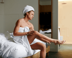 Mulher em uma toalha aplicando loção nas pernas
