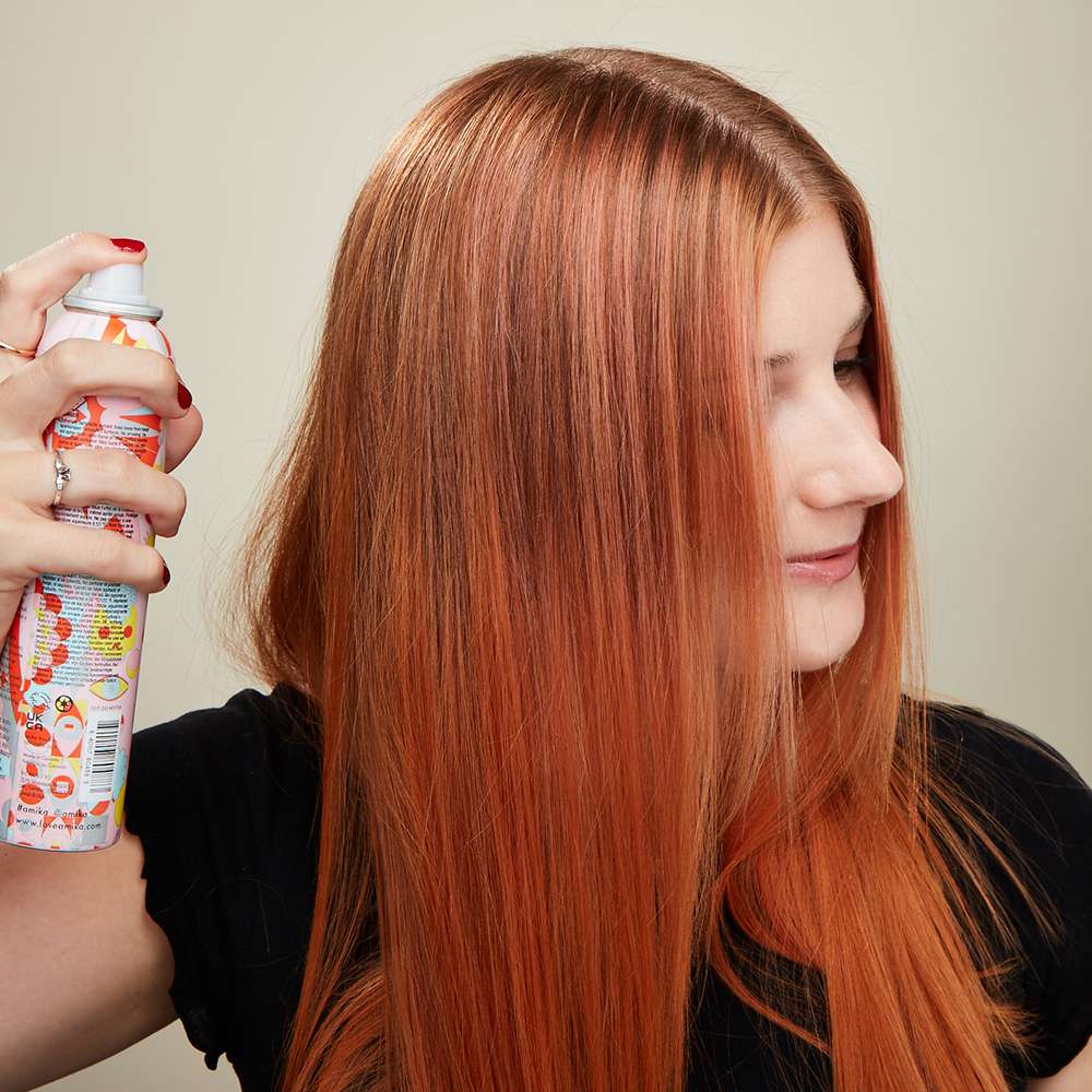 Uma mulher pulverizando o cabelo com um spray para brilhar