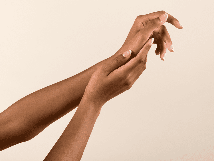 Manicure african a-americana, tocando suavemente a mão em um fundo bege