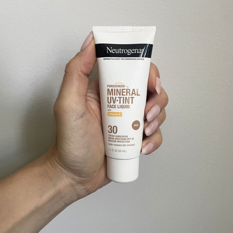 Mão segurando protetor solar facial líquido Neutrogena Purescreen+ Mineral UV Tint