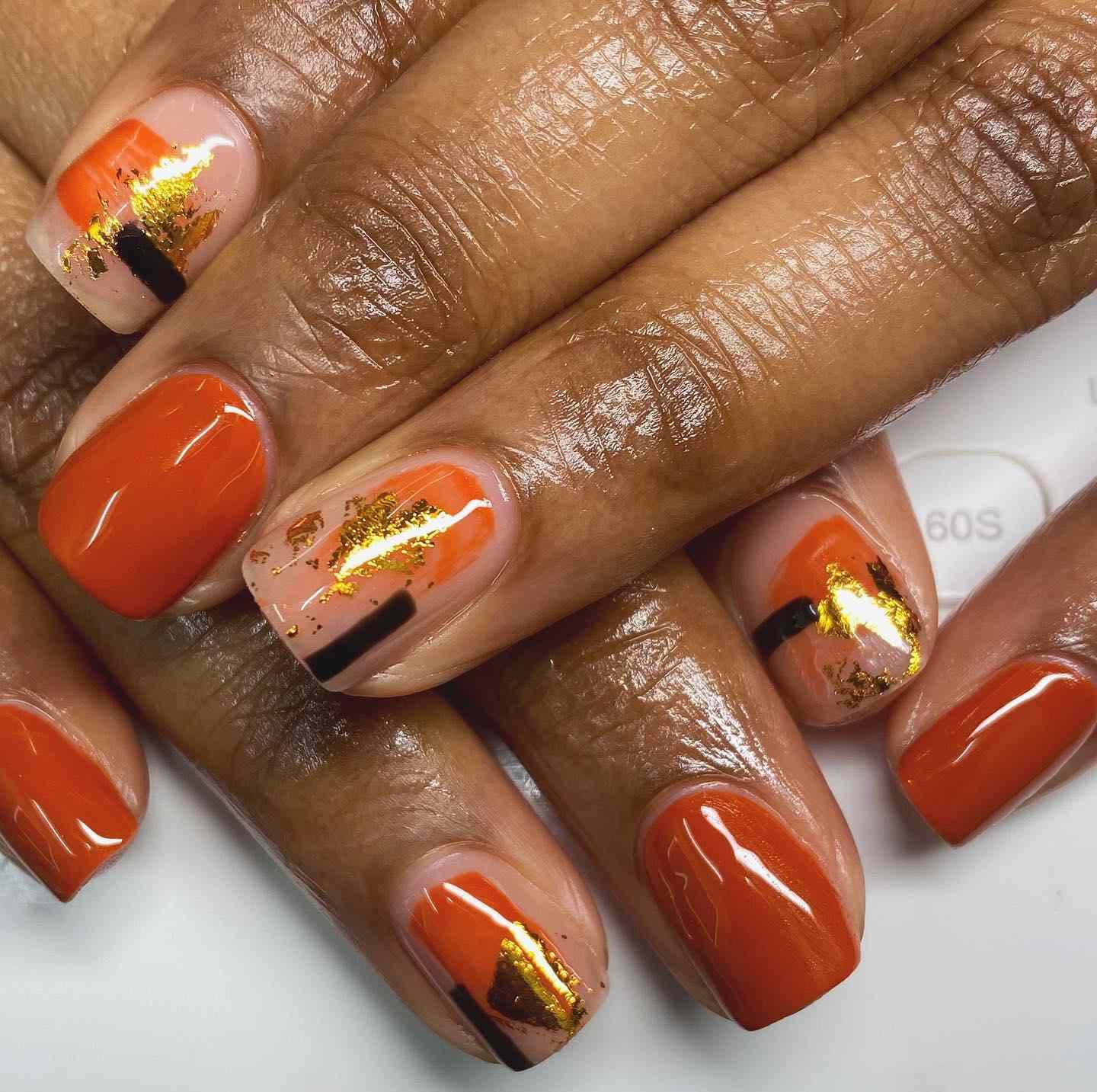 Nails quadrados curtos com arte abstrata de unhas laranja, preta e dourada da folha.