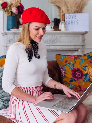 Mulher de boina vermelha e com um laptop em suas mãos
