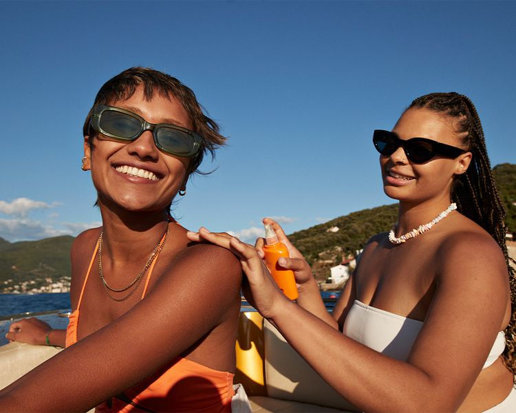 Uma mulher aplica um protetor solar nas costas de sua amiga